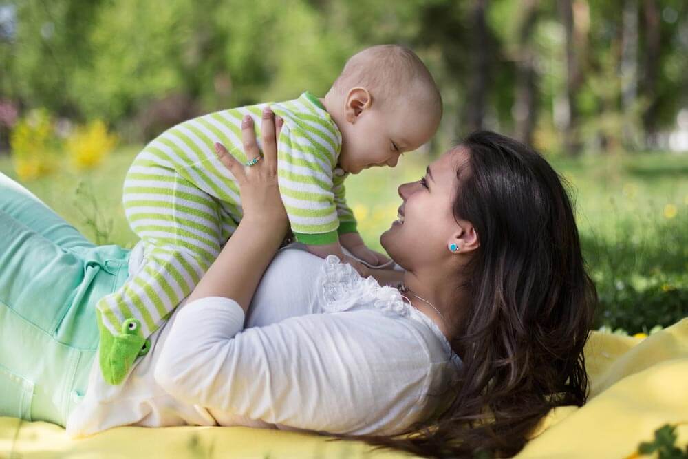 Happy mother lay with newborn baby on grass in park